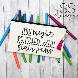 May include: A white canvas pencil case with a black zipper and a pink tassel. The case has the text "This might be filled with flair pens" printed on it. The case is filled with a variety of coloured pens.