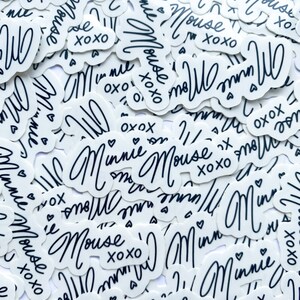 Op de afbeelding: Een close-up van een stapel witte stickers met zwarte letters. De stickers bevatten de tekst "Minnie Mouse" en "XOXO".
