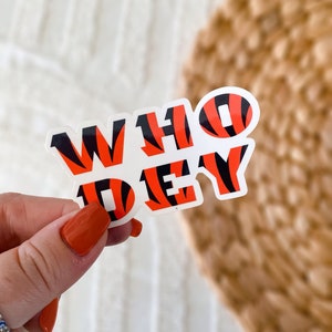 Op de afbeelding: Een witte sticker met de woorden "WHO DEY" in zwart en oranje tijgerstreep print.