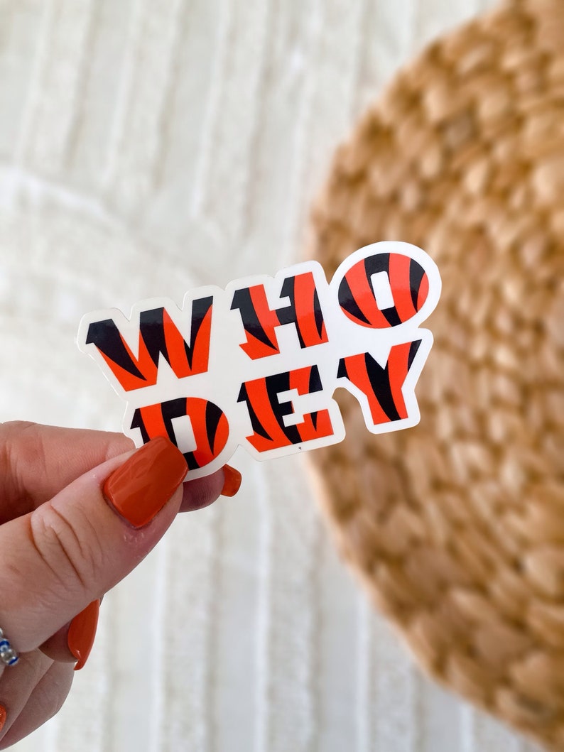 Op de afbeelding: Een witte sticker met de woorden "WHO DEY" in zwart en oranje tijgerstreep print.