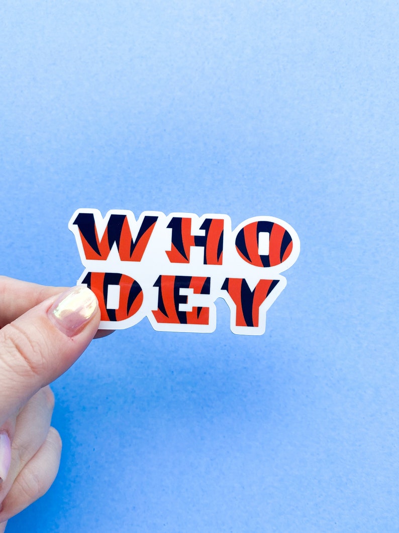 Op de afbeelding: Een witte sticker met de woorden "WHO DEY" in zwart en oranje tijgerstreep print.