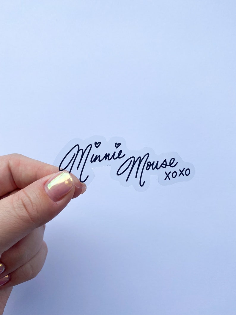 Op de afbeelding: Transparante sticker met zwarte schrijfletters die "Minnie Mouse xoxo" zeggen.