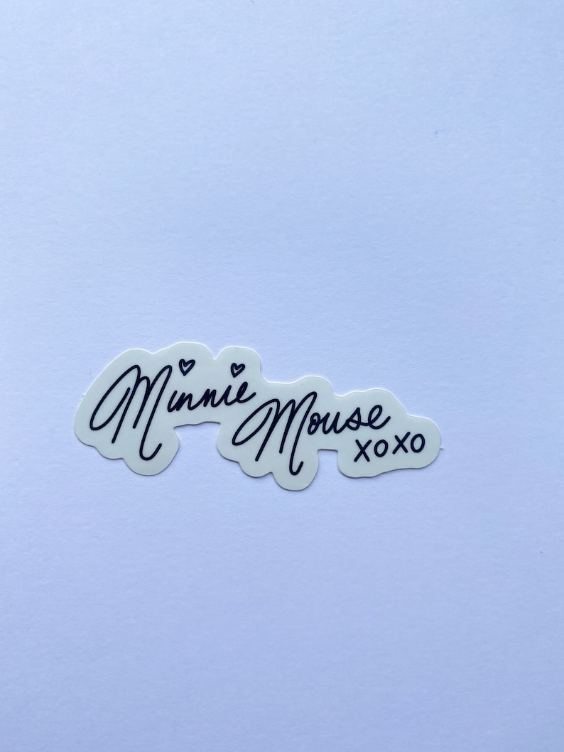 Op de afbeelding: Witte sticker met zwarte tekst die "Minnie Mouse xoxo" zegt.
