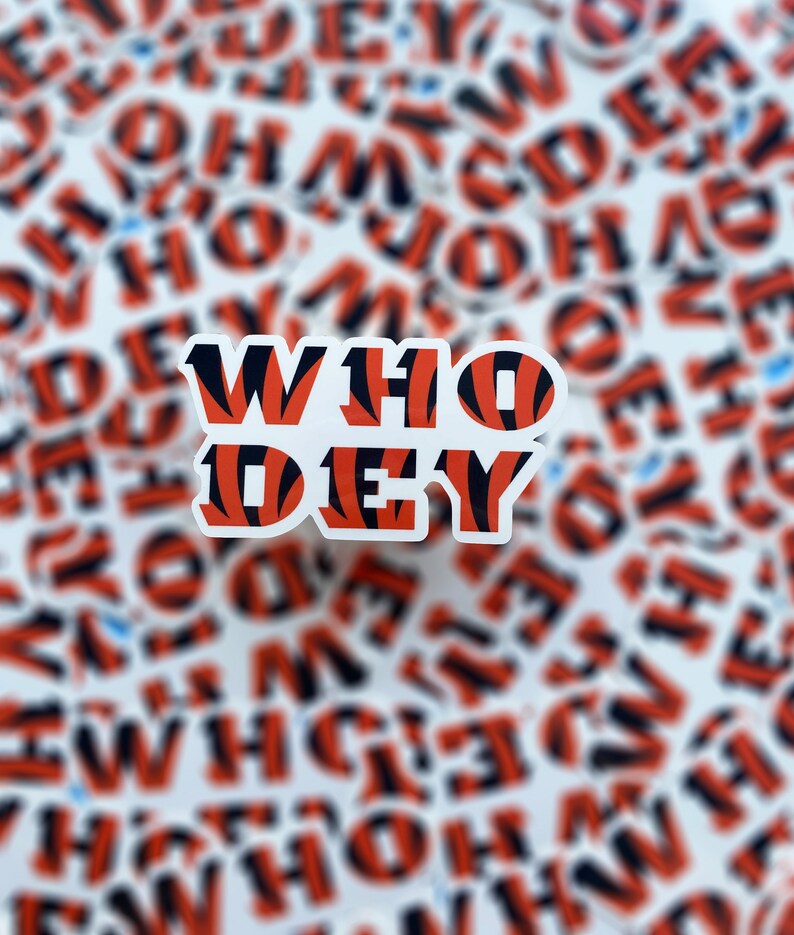Op de afbeelding: Een witte sticker met de woorden "WHO DEY" in zwarte en oranje tijgerstrepen. De sticker is omringd door veel andere stickers met hetzelfde ontwerp.