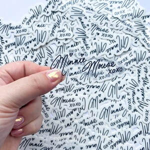 Op de afbeelding: Een close-up van een stapel witte stickers met zwarte tekst die "Minnie Mouse xoxo" zegt.