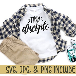 May include: A white t-shirt with the text "TINY disciple" in black lettering. The shirt is displayed on a model with a plaid shirt, khaki pants, and blue sneakers.