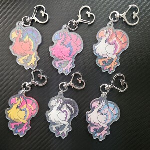 May include: A collection of six keychains featuring a bird design with various color schemes. Each keychain has a silver-colored clasp. The birds are in shades of red, pink, yellow, white, and blue, with rainbow, striped, and solid-color details.