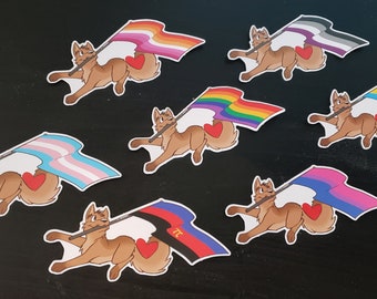 May include: A collection of stickers featuring a cartoon dog carrying various Pride flags. Each dog has a red heart on its side. The flags represent different LGBTQ+ identities, including lesbian, transgender, and bisexual.