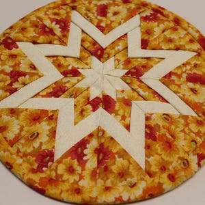 May include: A round, quilted hot pad with a star design. The star is made of white fabric and the background is a yellow fabric with red and yellow flowers.