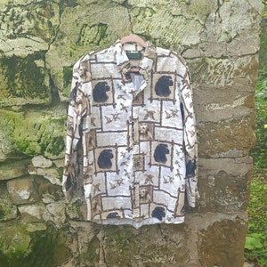 May include: A white long-sleeved button-down shirt with a brown and black print of dogs and birds.
