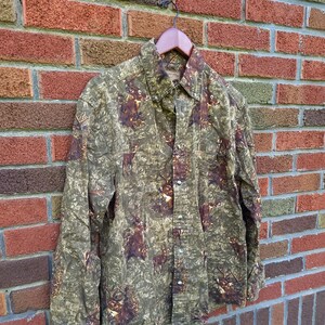 May include: A long-sleeved button-up shirt with a camouflage pattern featuring deer silhouettes. The shirt is brown, green, and orange.