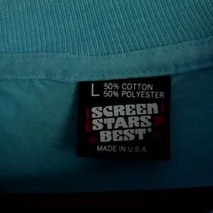 May include: A blue t-shirt tag with white text that reads "50% Cotton 50% Polyester" and "Screen Stars Best" in red. The tag also says "Made in U.S.A."