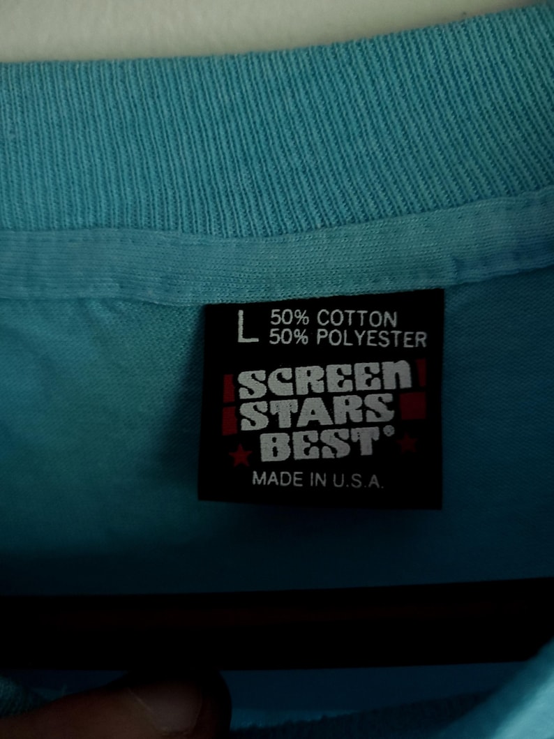 May include: A blue t-shirt tag with white text that reads "50% Cotton 50% Polyester" and "Screen Stars Best" in red. The tag also says "Made in U.S.A."