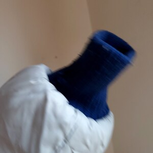 May include: A white quilted jacket with a navy blue ribbed knit cuff. The jacket appears to be made of a smooth, possibly water-resistant material. The cuff is a darker shade of blue.