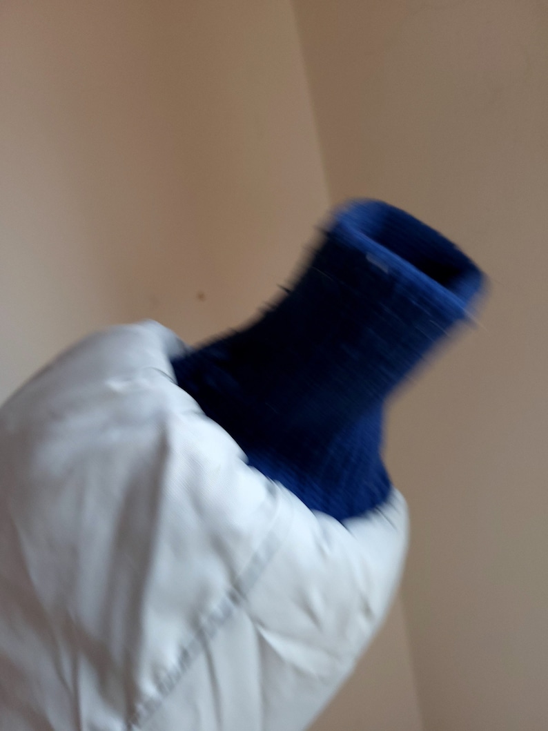 May include: A white quilted jacket with a navy blue ribbed knit cuff. The jacket appears to be made of a smooth, possibly water-resistant material. The cuff is a darker shade of blue.