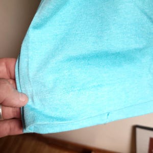 May include: Close-up of the bottom hem of a light blue t-shirt. The fabric is soft and has a slight texture.