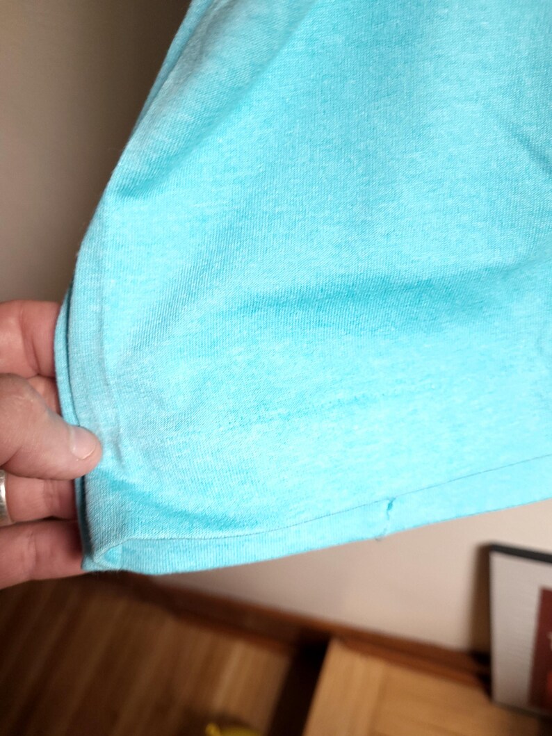 May include: Close-up of the bottom hem of a light blue t-shirt. The fabric is soft and has a slight texture.