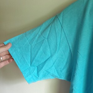 May include: A turquoise short-sleeved t-shirt made of a soft, lightweight fabric. The shirt is a solid color with no graphics or designs.