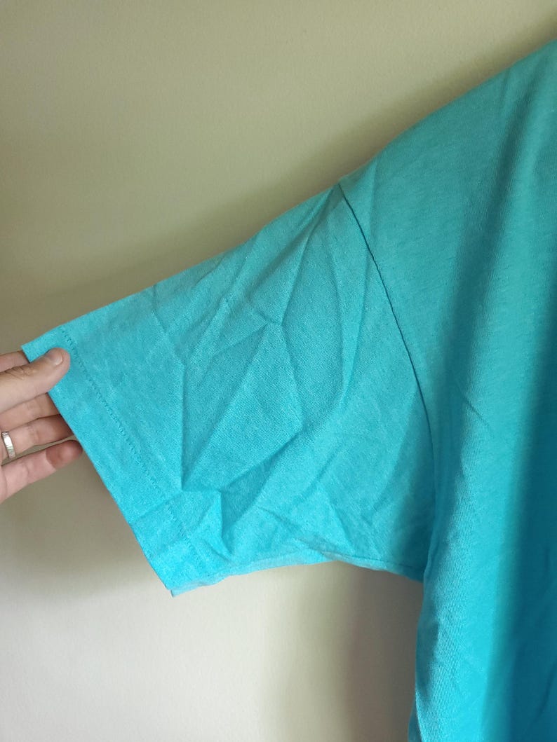 May include: A turquoise short-sleeved t-shirt made of a soft, lightweight fabric. The shirt is a solid color with no graphics or designs.