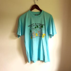 May include: A light blue t-shirt with a graphic of two cartoon bears playing guitars. The text on the shirt reads "Shorty & Lorene two for the show".