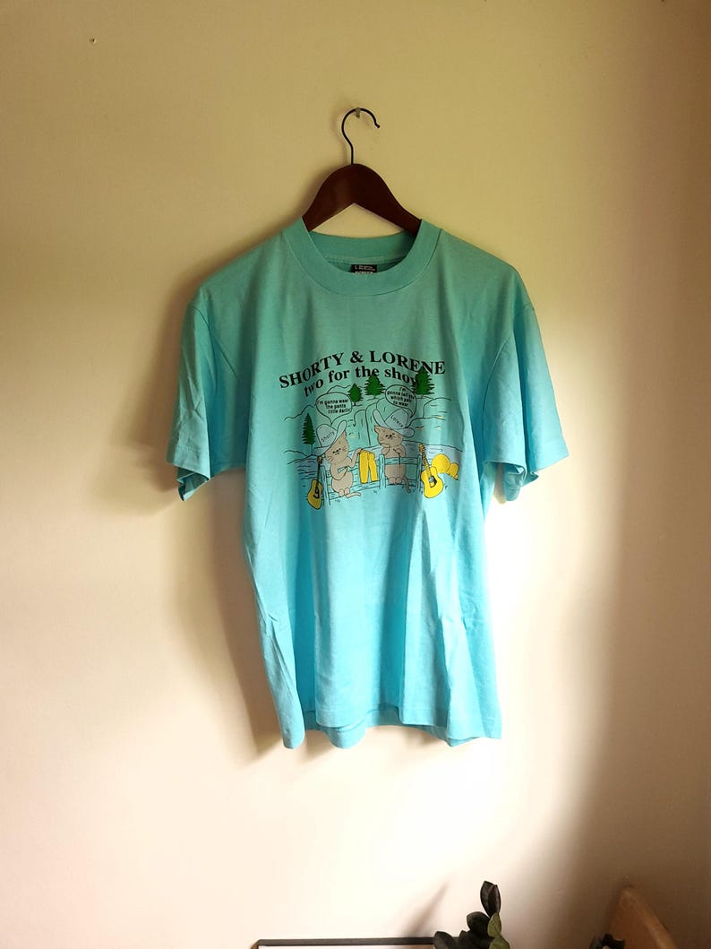May include: A light blue t-shirt with a graphic of two cartoon bears playing guitars. The text on the shirt reads "Shorty & Lorene two for the show".