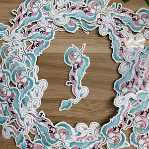 May include: A collection of stickers featuring a whimsical, stylized dragon with blue and pink scales. The dragon is depicted in various poses, including flying, swimming, and resting. The stickers are perfect for adding a touch of fantasy to any surface.