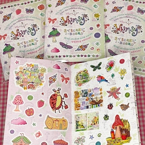 May include: A collection of open sticker books featuring the title "Whimsy Sticker Book" on the covers. The books contain various stickers with illustrations of mushrooms, butterflies, and other whimsical designs. The background is a pink and white checkered pattern.