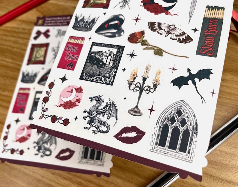 May include: A sheet of stickers featuring a variety of gothic and fantasy themed designs. The stickers include a dragon, a castle, a candle holder, a moth, a crown, a window, and a heart. The stickers are printed on white paper with a red border.
