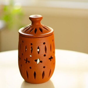 May include: A terracotta jar with a lid, featuring intricate cut-out designs. The jar is a light brown colour and has a smooth, matte finish.