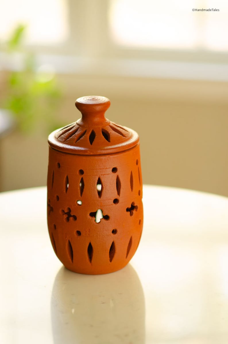 May include: A terracotta jar with a lid, featuring intricate cut-out designs. The jar is a light brown colour and has a smooth, matte finish.