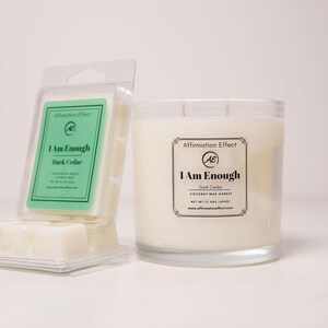 May include: A candle and wax melts set. The candle is in a clear glass jar with a white wax and two wicks. The wax melts are in a clear plastic container. Both products have labels that read "I Am Enough Dark Cedar".
