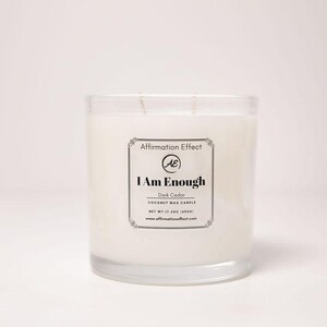 May include: A clear glass candle jar filled with white wax. The label reads "I Am Enough" and "Dark Cedar Coconut Wax Candle". The candle weighs 17.5 oz (496g). The brand name is "Affirmation Effect".