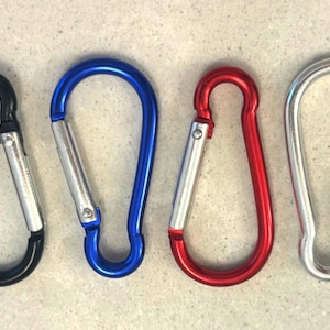 May include: Four carabiner clips arranged in a row, featuring a black, a blue, a red, and a silver metal finish. Each carabiner has a spring-loaded gate mechanism that allows for quick attachment and secure closure for various utility purposes.
