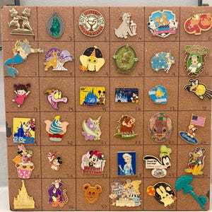 May include: A collection of thirty-five assorted Disney character enamel pins arranged in a grid on a cork board. The pins feature various figures including Mickey Mouse, Tinker Bell, Stitch, and Elsa, with some displaying text like 50, August, and 2022.