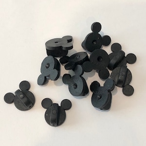May include: A group of ten black plastic Mickey Mouse head shaped pin backs. The pin backs are all the same size and shape, and they are arranged in a random pattern.