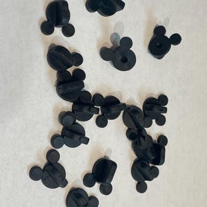 May include: A collection of black plastic Mickey Mouse pin backs. The pin backs are used to attach pins to clothing or other items.