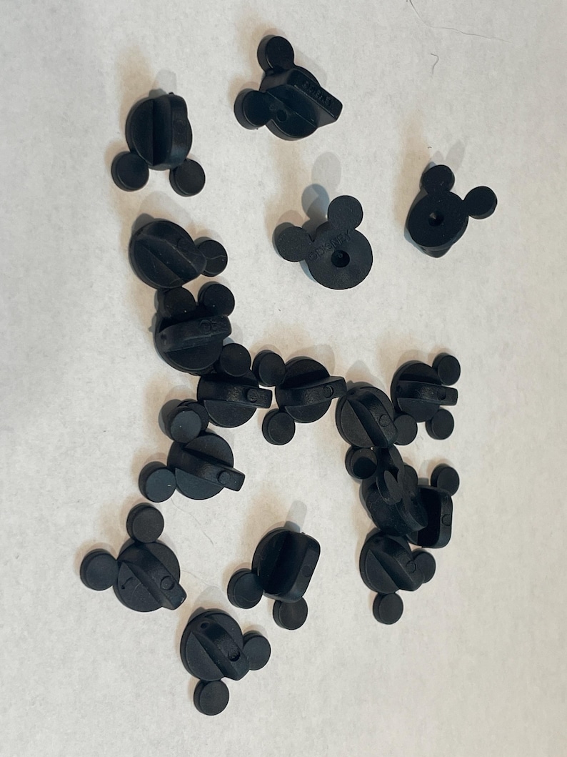 May include: A collection of black plastic Mickey Mouse pin backs. The pin backs are used to attach pins to clothing or other items.