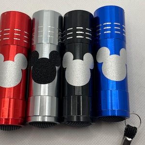 May include: Four small flashlights with Mickey Mouse ears. The flashlights are red, silver, black, and blue.