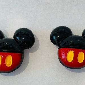 May include: Two black and red Mickey Mouse head shaped buttons with yellow eyes.
