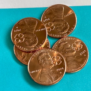 May include: Five copper-colored US pennies with a four-leaf clover design. Each coin reads "In God We Trust", "Liberty", and "2024 D".