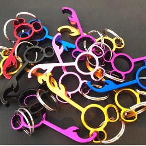 May include: A collection of colorful metal bottle openers with key rings. The openers are shaped like a Mickey Mouse head with three circles. The colors include red, blue, gold, black, and purple.