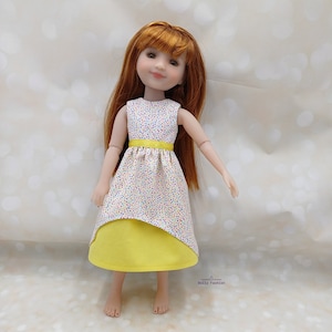 May include: A doll wearing a yellow and white polka dot dress with a yellow sash. The doll has long red hair and is wearing a white dress with a yellow sash.