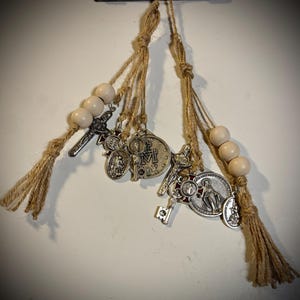 May include: Religious-themed hanging ornaments featuring silver-toned charms and wooden beads. The charms include crosses, medallions, and keys, suspended from natural twine. The ornaments are designed for decorative purposes.