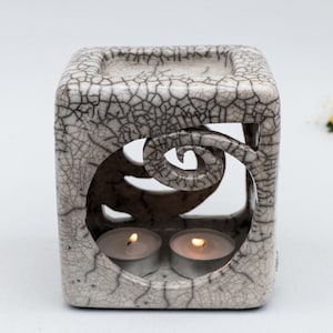 Cube shape ceramic oil burner in white color with black smoked crackles, internal top bowl for the essential oil, two spiral shape cuts in the sides opposite, the front one bigger, to load the candle. It is one of a kind.