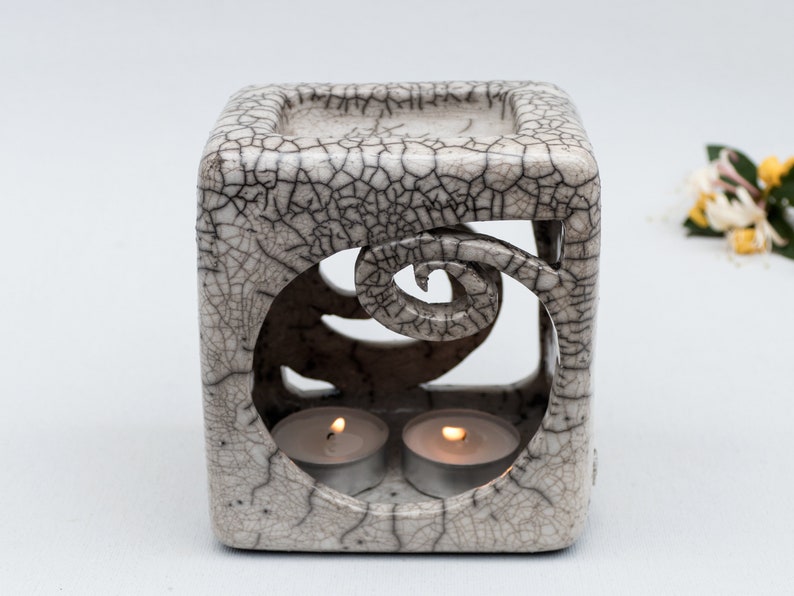Cube shape ceramic oil burner in white color with black smoked crackles, internal top bowl for the essential oil, two spiral shape cuts in the sides opposite, the front one bigger, to load the candle. It is one of a kind.