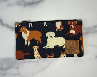 May include: A navy blue zippered pouch featuring a repeating pattern of various dog breeds in shades of brown, white, and tan. The pouch has a small cork tag with the text "Seriously Dog Designs".
