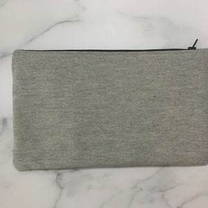 May include: A rectangular, light gray zippered pouch made of a textured fabric. The zipper is black, and the pouch is closed. The pouch is a neutral color and could be used for various purposes.