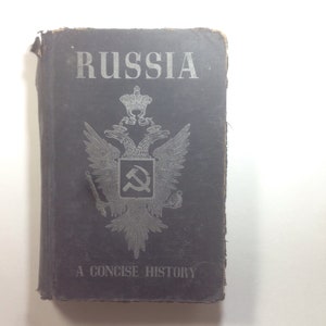 May include: A black book with the title "Russia: A Concise History" on the cover. The cover features a silver-colored double-headed eagle with a hammer and sickle in the center.