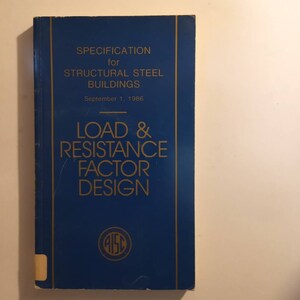 May include: A blue book with gold lettering titled "Specification for Structural Steel Buildings Load & Resistance Factor Design" with the date September 1, 1986. The book has a gold circle with the letters "AISC" in the center.
