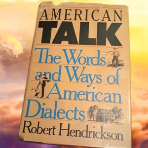 May include: A vintage book titled "AMERICAN TALK" with the subtitle "The Words and Ways of American Dialects" by Robert Hendrickson. The cover is tan with black and blue text and illustrations of people and a house.